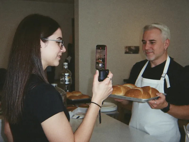 Ana che riprende con il telefono sullo stabilizzatore un panettiere che le mostra il pane appena sfornato